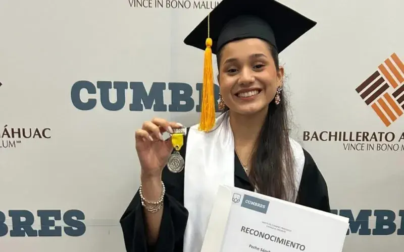 Estudiante en ceremonia de graduación mostrando medalla y diploma de "Reconocimiento" del Bachillerato.